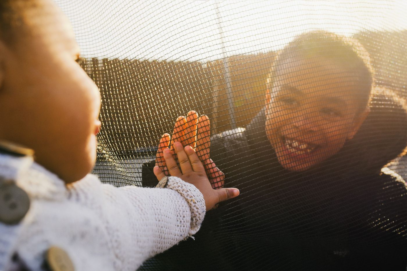 Two children high-fiving through a trampoline net in golden light