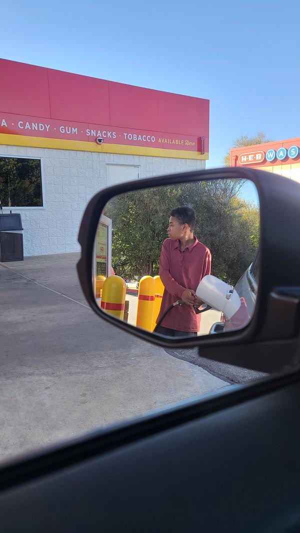 Teen pumping gas, seen in a side mirror
